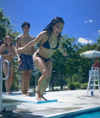 A young woman leaps off a diving board into a bright blue pool, sharp and cool on AQUA DV.