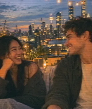 A couple laughs on a rooftop at dusk with the city behind them, letterboxed like cinema mode on MATINEE.