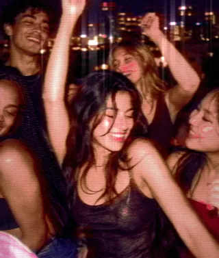 Friends dance at a night party, one holding up a pink glow stick, hot and saturated on NITELIFE.
